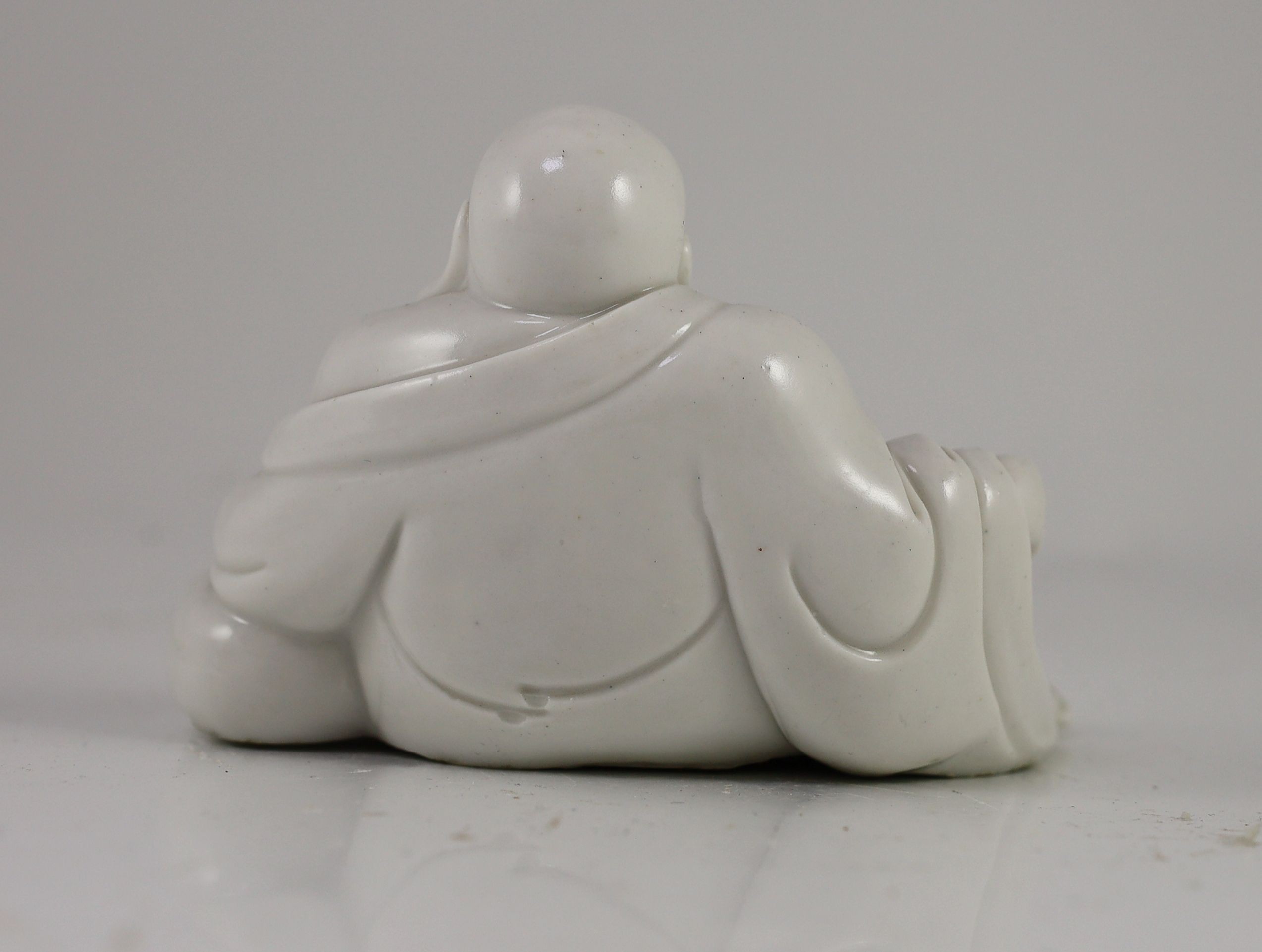 CORRECTION CIRCA 1900 A Chinese blanc-de-chine reclining figure of a smiling Budai, Dehua kilns, 15cm wide
